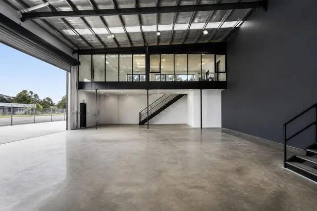 Warehouse 02 interior — Inside a typical tenancy — sealed concrete slab, clear-span steel portal frame with up to 7.5m clearance, and the glazed mezzanine office above the entry.